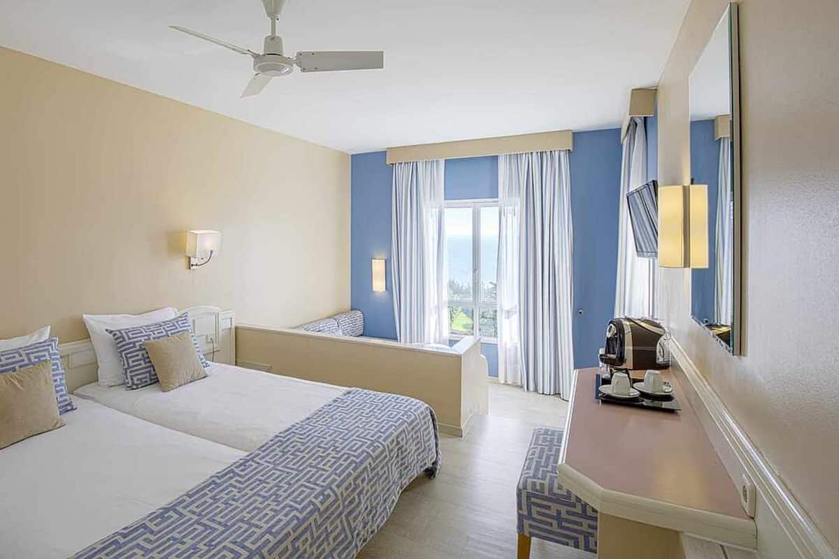 Une chambre d’hôtel avec deux lits, un bureau, un ventilateur de plafond et une vue sur l’extérieur.