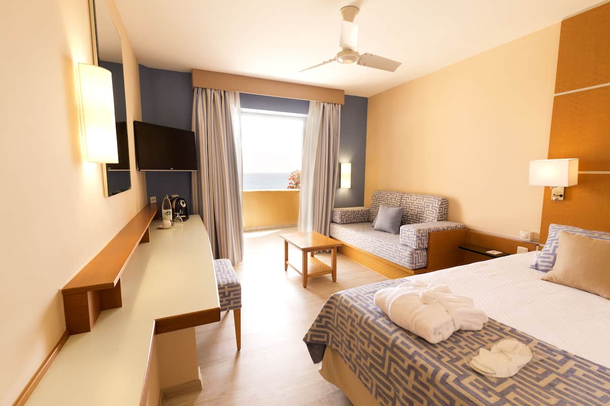 Une chambre d’hôtel équipée d’un lit, d’un bureau, d’un canapé, d’un ventilateur de plafond et d’une fenêtre avec des rideaux.