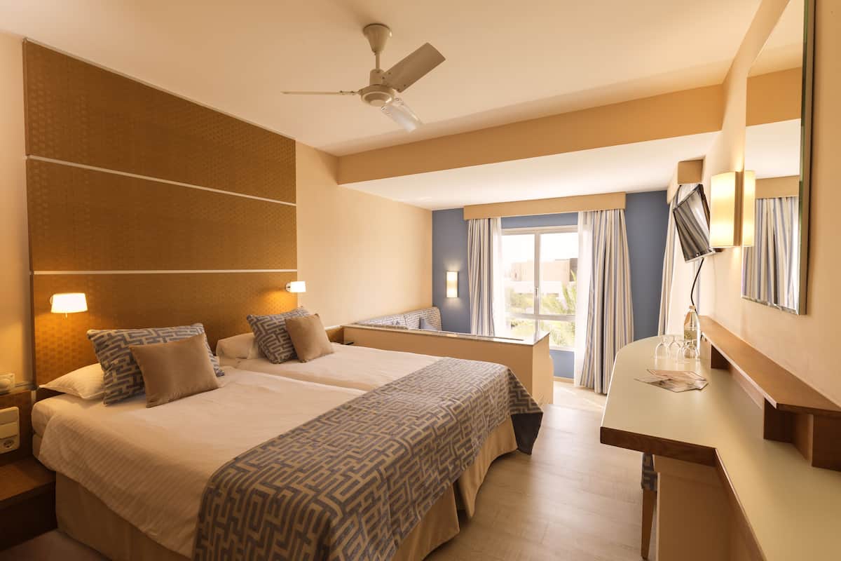 Une chambre d’hôtel avec deux lits, un bureau, un ventilateur de plafond et une fenêtre avec des rideaux.