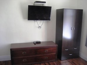 Una stanza con una TV a schermo piatto montata a parete, un comò in legno con cassetti e un'alta credenza scura.