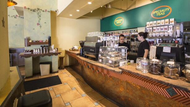 Interior de una cafetería con mostrador, máquinas de espresso y una variedad de granos y recipientes de café.