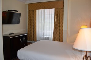 A hotel room with a bed, a desk with a television, and a window with curtains. - Post Hotel (San Francisco)