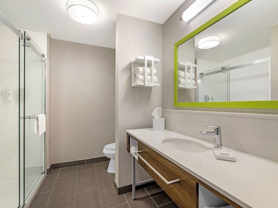 Un baño moderno con cabina de ducha de vidrio, un lavabo blanco con tocador de madera y un espejo con marco verde.