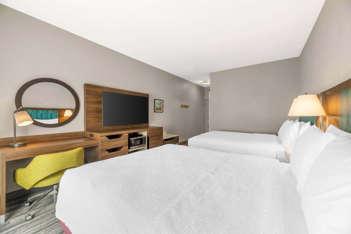 A hotel room with two beds, a desk with a computer, a TV, and a lamp.