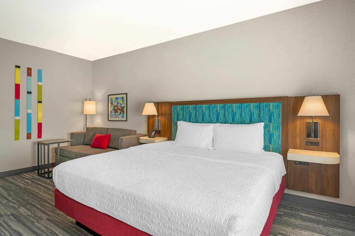 A hotel room with a large bed, two bedside tables, a sofa, and a wall with colorful vertical stripes.