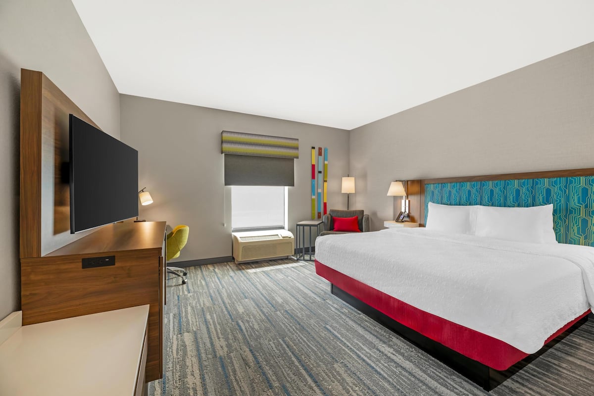 A hotel room with a large bed, a flat-screen TV, a desk, and a chair.