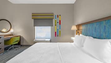 A hotel room with a large bed, a desk with a chair, a window with a view, and a wall with a geometric pattern.