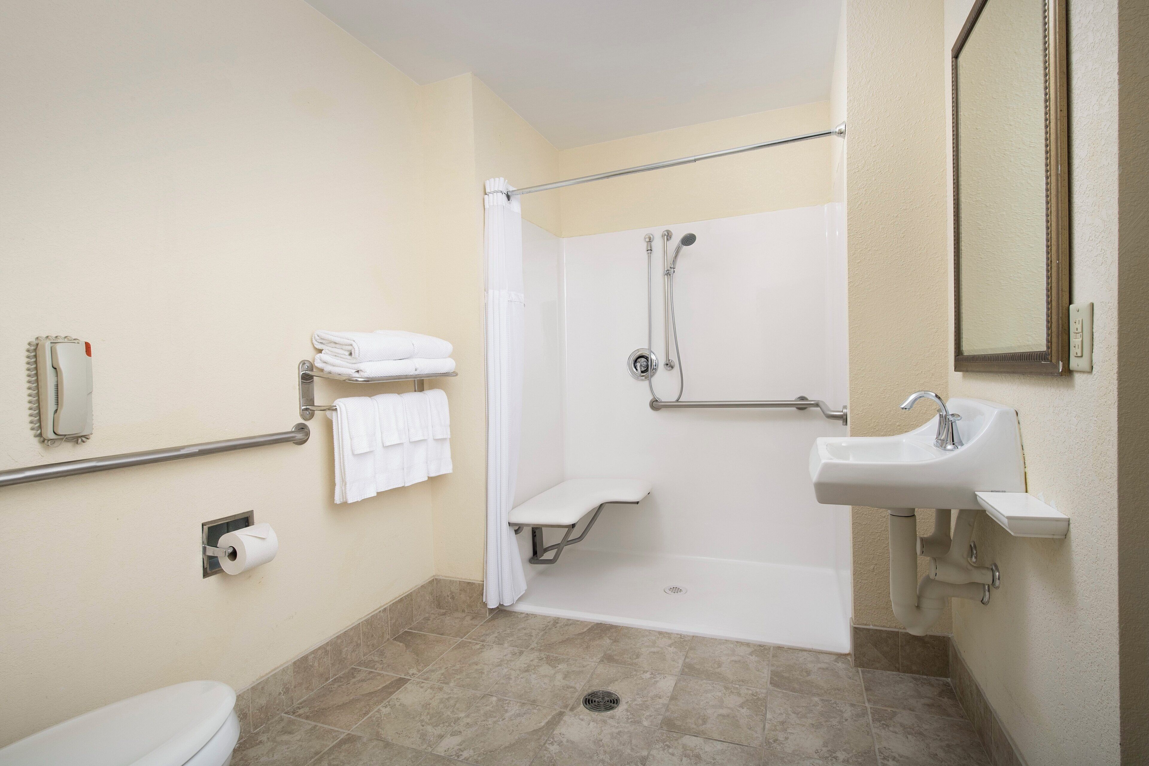 A bathroom with a toilet, a shower with a grab bar, a sink, and a towel rack.