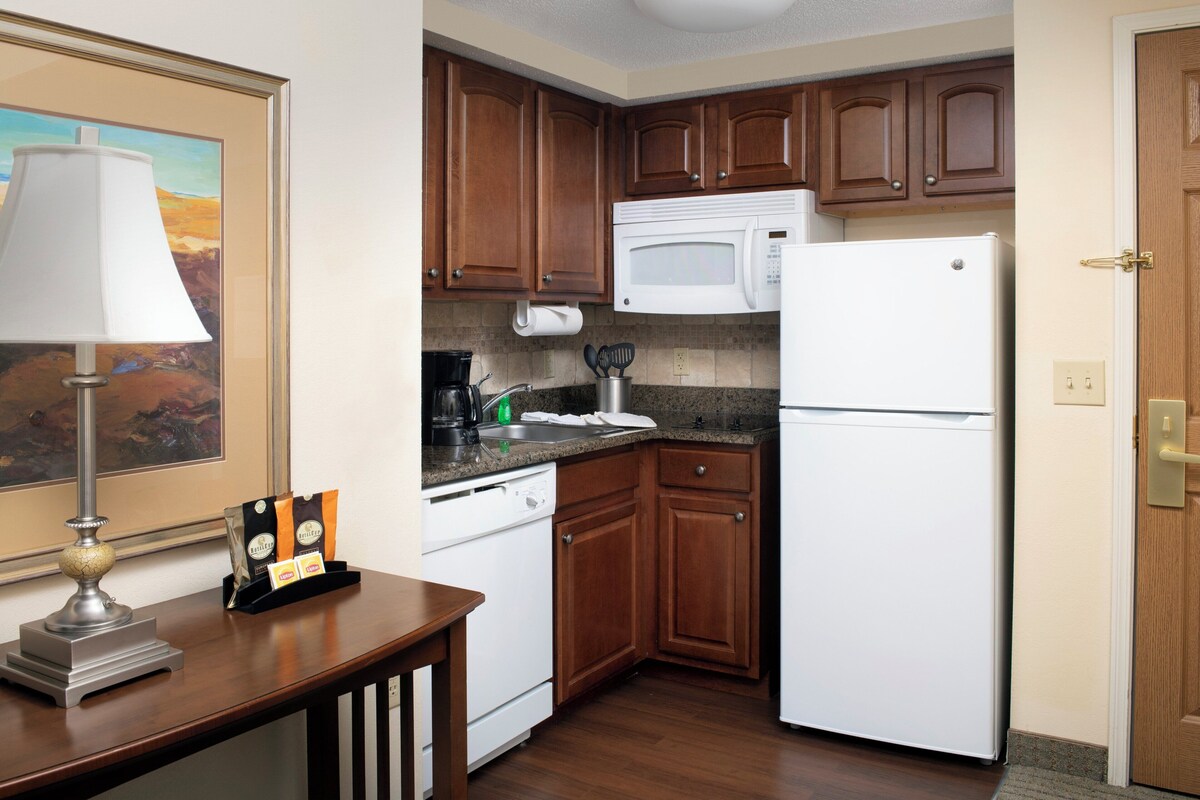 A kitchen with wooden cabinets, a white microwave, a white refrigerator, a coffee maker, and a framed picture on the wall.