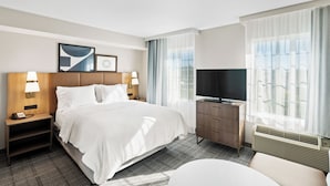 A hotel room with a large bed, two bedside tables with lamps, a dresser, a television, and a window with curtains. - Staybridge Suites North Brunswick by IHG (North Brunswick)