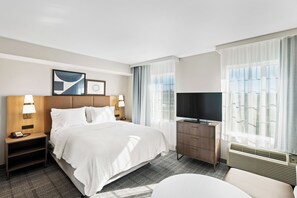 A hotel room with a large bed, two bedside tables with lamps, a dresser, a television, and a window with curtains. - Staybridge Suites North Brunswick by IHG (North Brunswick)