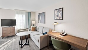A modern hotel room with a sofa, a small table, a desk with a lamp, a TV, and artwork on the walls. - Staybridge Suites North Brunswick by IHG (North Brunswick)