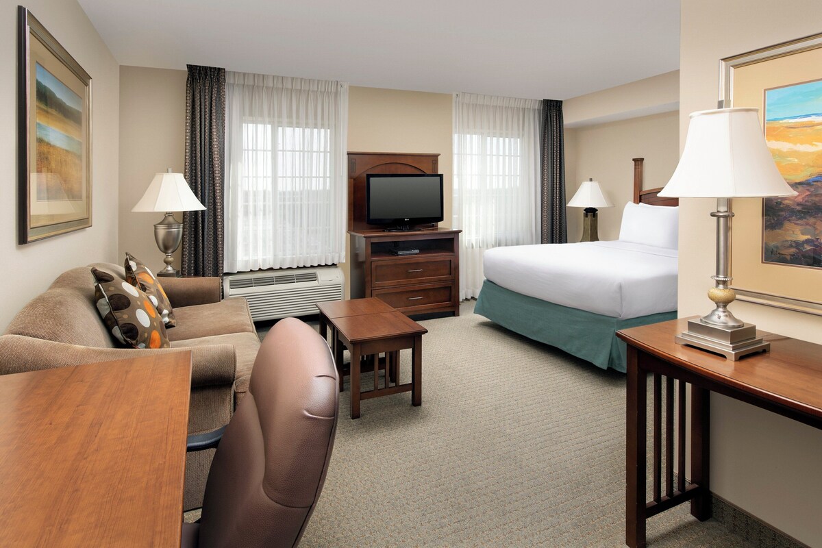 A hotel room with a bed, a TV, a desk, a chair, a lamp, and a painting.