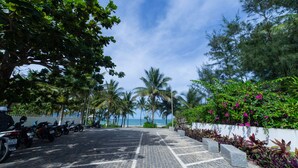 A paved pathway leading to a beach with parked motorcycles and lush greenery. - Gold Coast Da Nang Hotel (Da Nang)