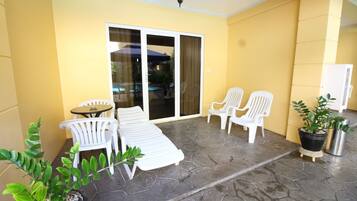 A patio area with white plastic chairs and a table, a sliding glass door leading to a pool, and potted plants.