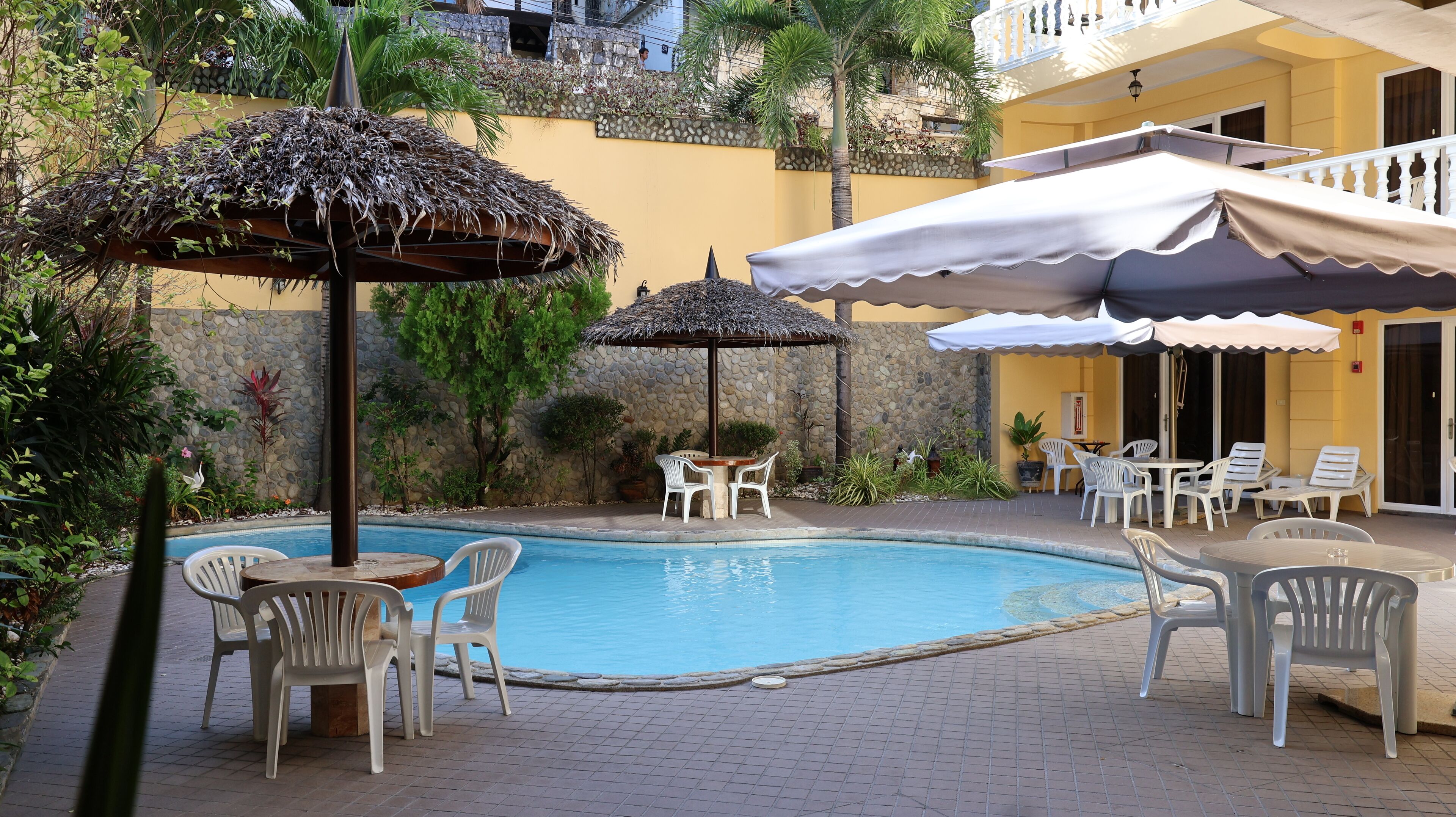A pool area with chairs and umbrellas, surrounded by plants and a stone wall.