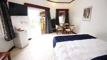 A hotel room with a bed, a desk, and a chair. There is a television mounted on the wall, and a window with curtains.