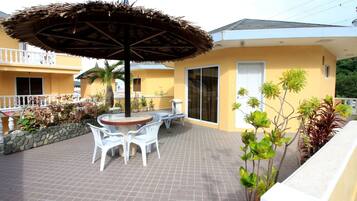 A patio with a round table and chairs, an umbrella, and potted plants.
