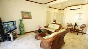 A living room with a television, a green vase, wicker furniture, and a dining area with chairs and a table. - Mermaid Resort Puerto Galera (Puerto Galera)