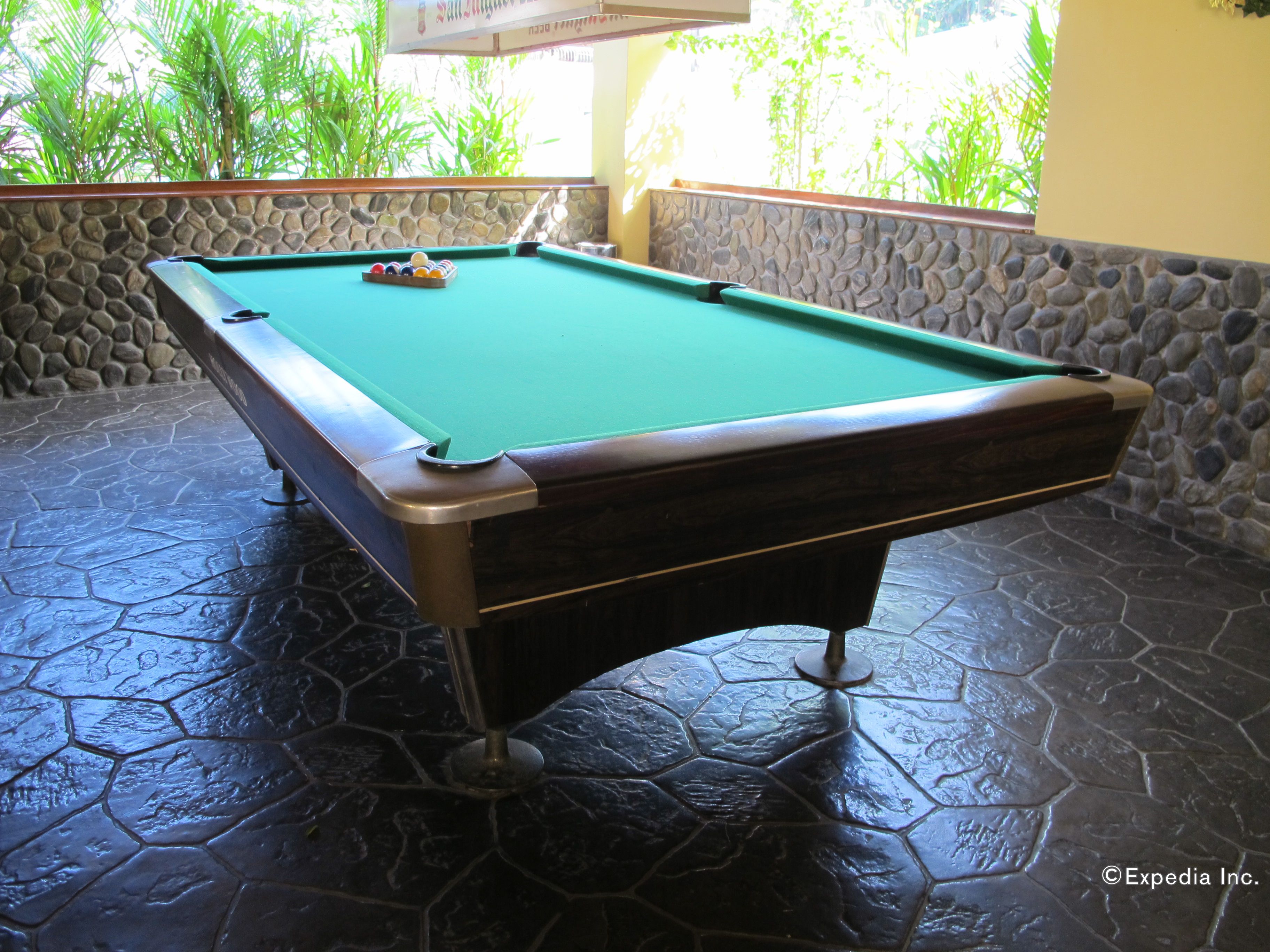 A pool table with a stone-tiled floor and a stone wall backdrop.