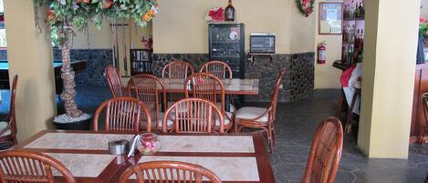 Een restaurant met houten tafels en stoelen, een stenen muur en een decoratieve plant.