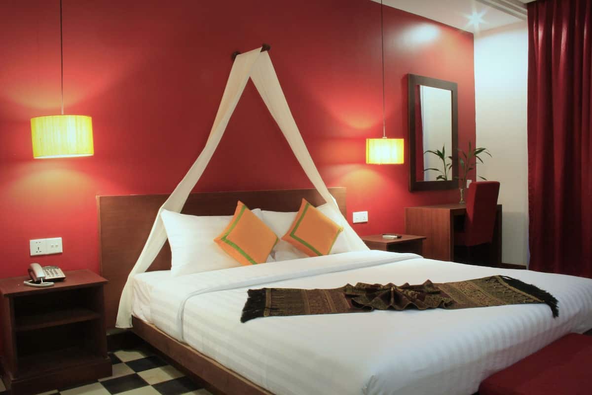 Una habitación de hotel con cama, mesitas de noche, teléfono, espejo y planta.
