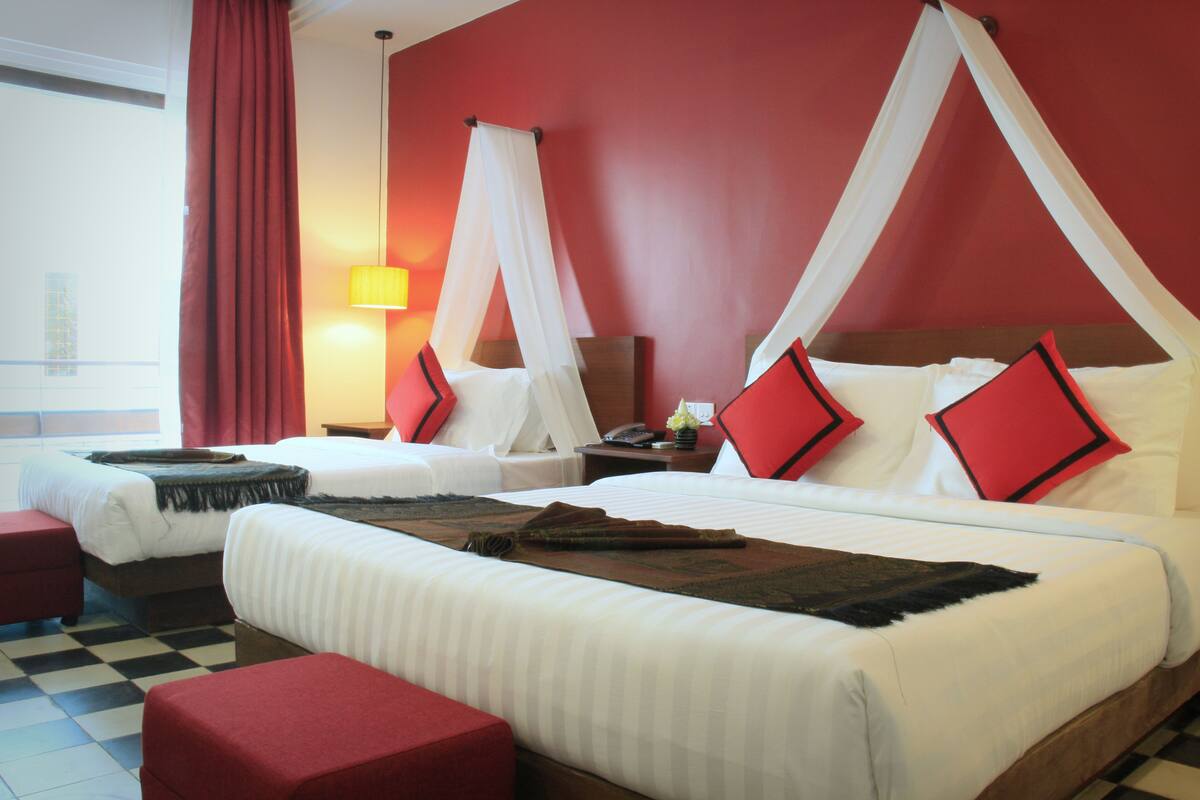 Habitación de hotel con dos camas, ropa de cama roja y blanca, suelo a cuadros y una cortina roja.