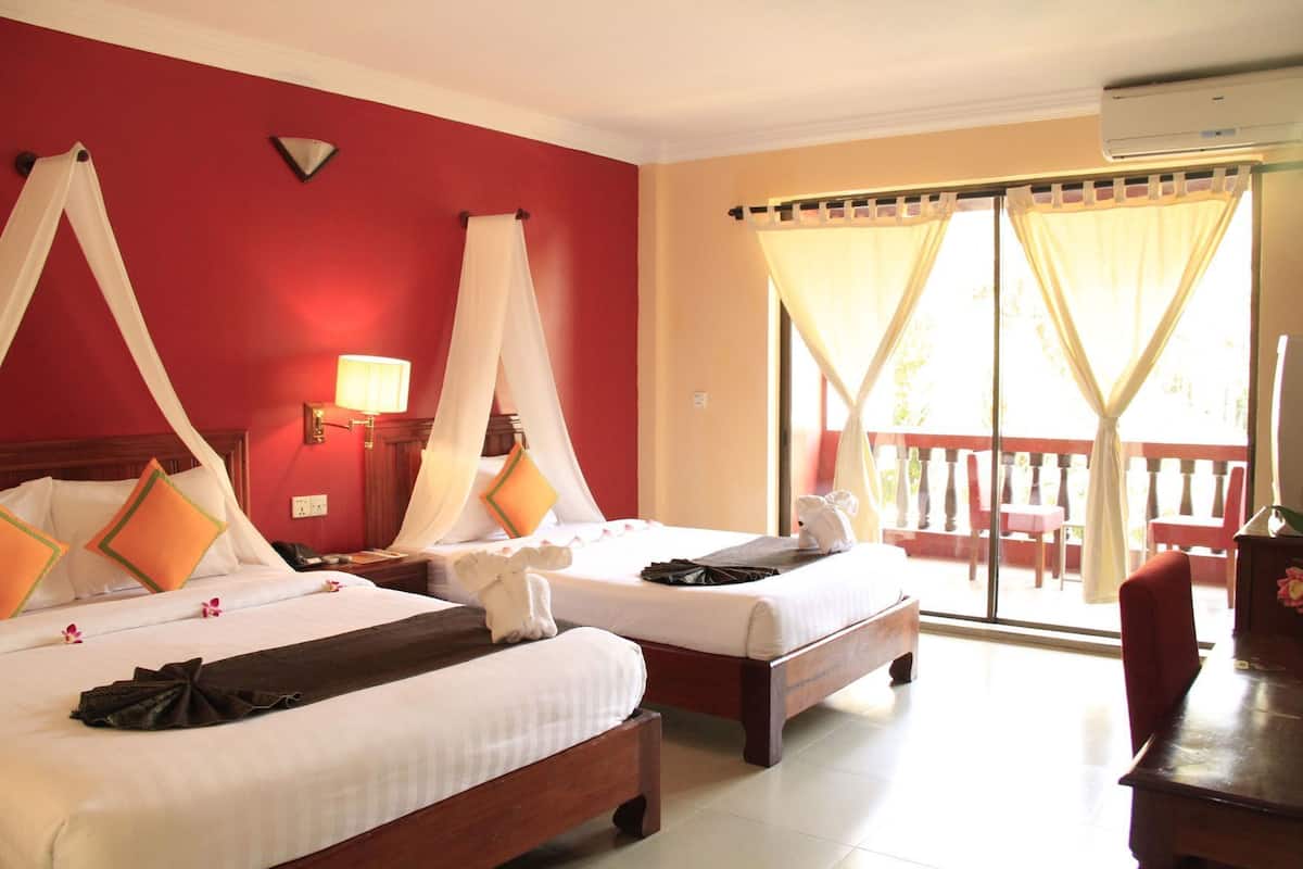 Habitación de hotel con dos camas, un balcón con barandilla roja y un equipo de aire acondicionado.