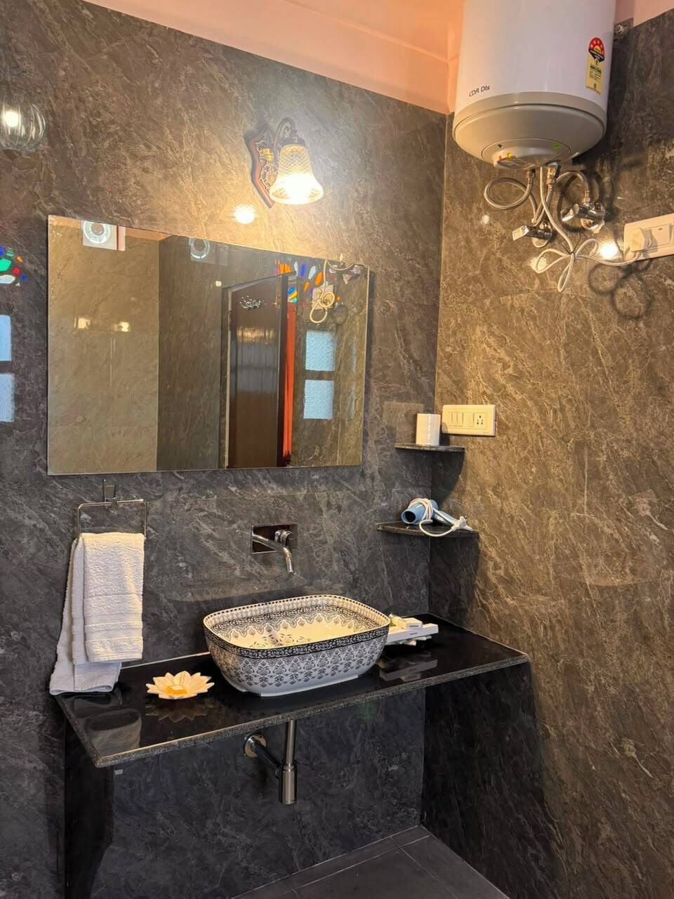 A modern bathroom with a black marble sink, a large mirror, and a wall-mounted heater.