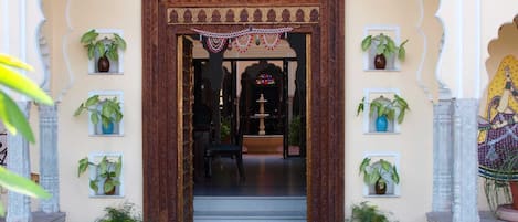 Una entrada ornamentada con un arco decorativo, plantas en macetas y una escalera que conduce a un espacio interior.