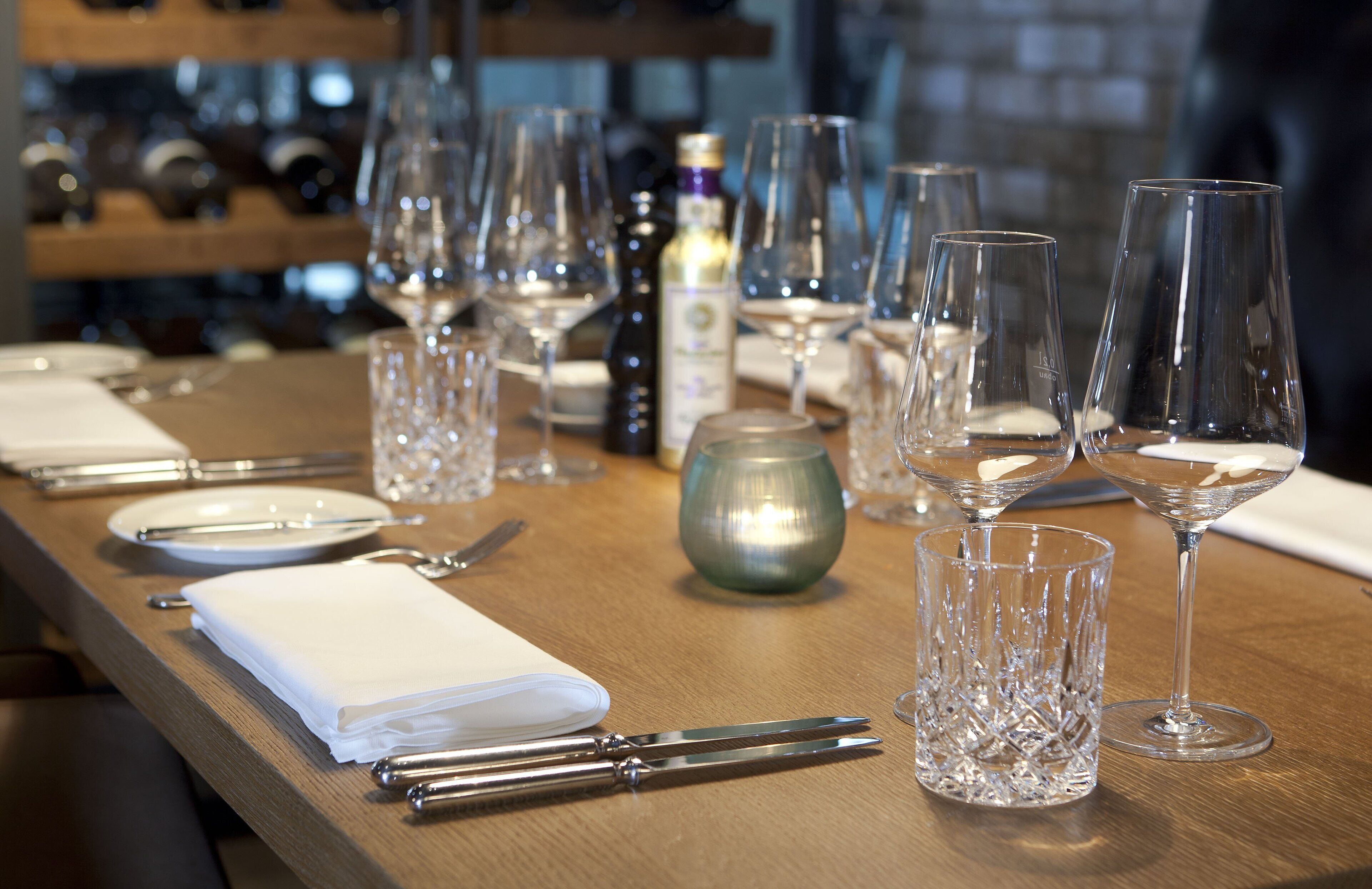 A dining table set with wine glasses, plates, cutlery, and a bottle of wine.