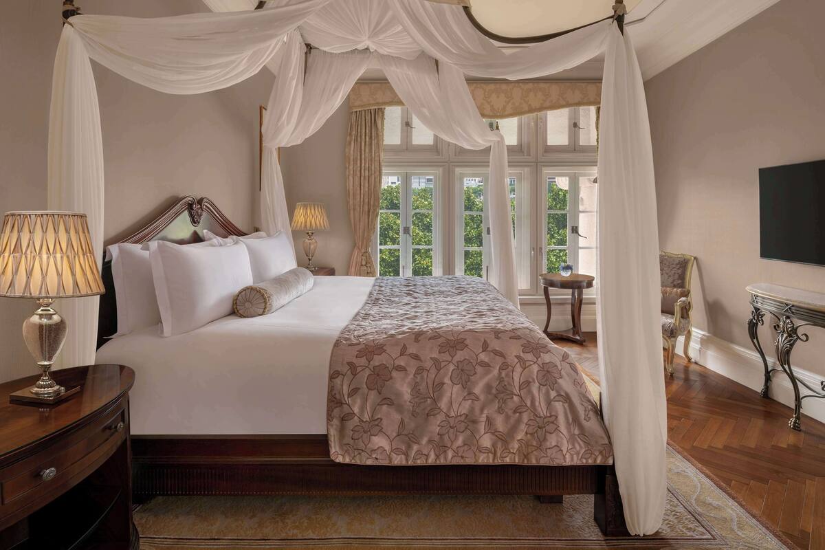 Ein Himmelbett mit floralem Überwurf, Nachttischlampen und Blick auf Grün außerhalb.