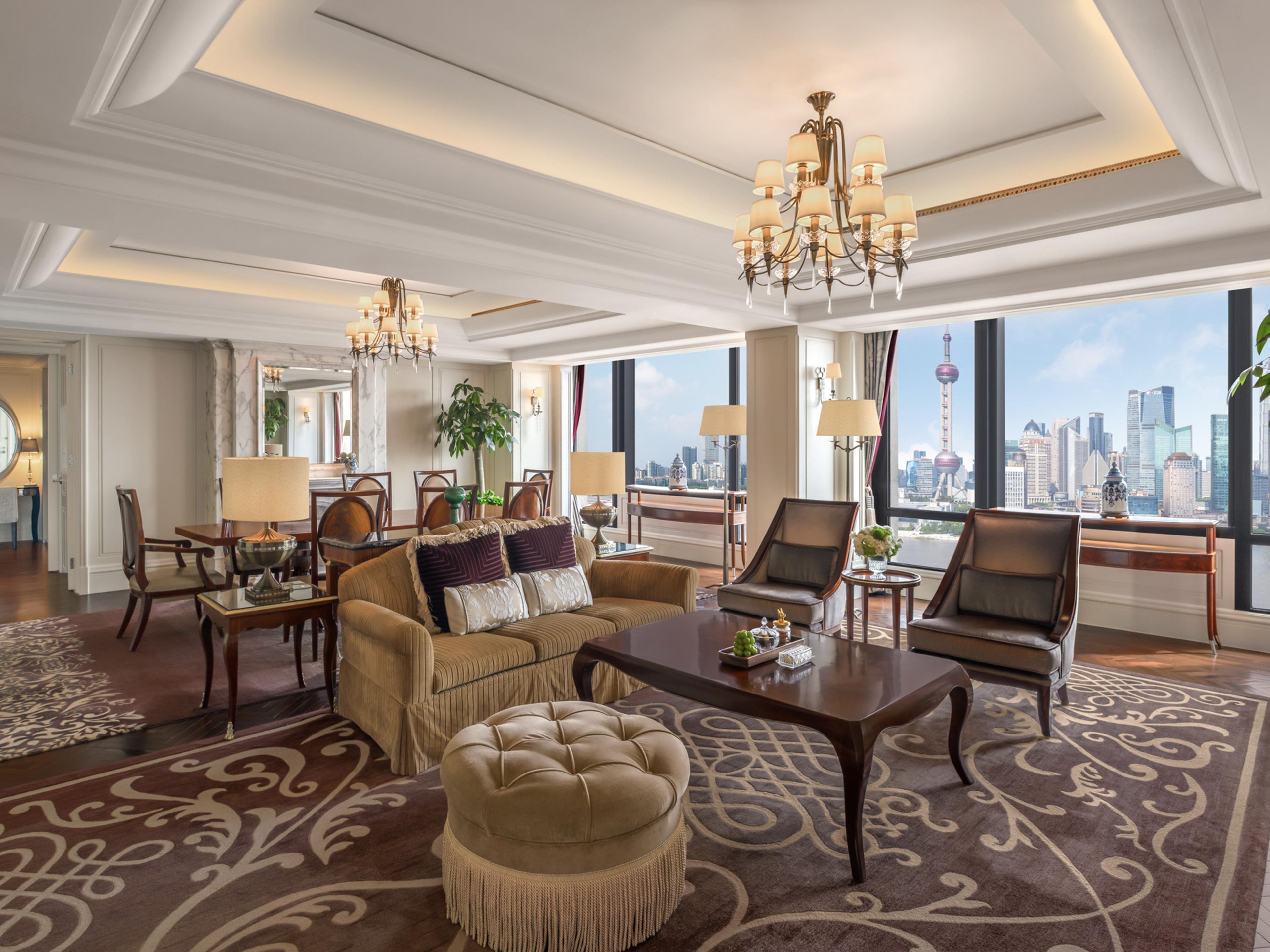 A spacious hotel room with a city view, a large chandelier, and a plush sofa set.