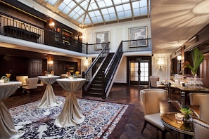 Un hall d’hôtel spacieux, doté d’un haut plafond, d’un escalier central et de plusieurs espaces aménagés pour s’asseoir.