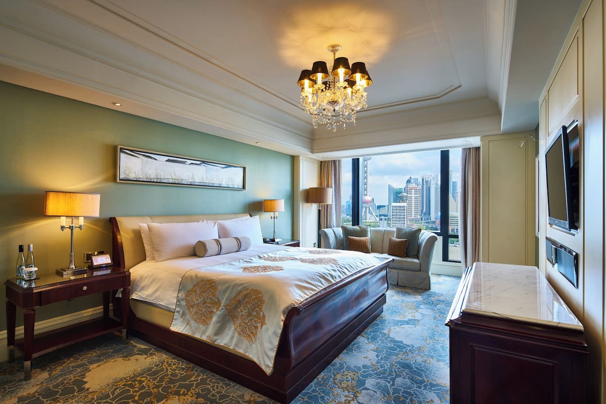 Ein geräumiges Hotelzimmer mit einem großen Bett, einer Sitzecke mit Blick auf die Stadt und einem Fernseher auf der rechten Seite.
