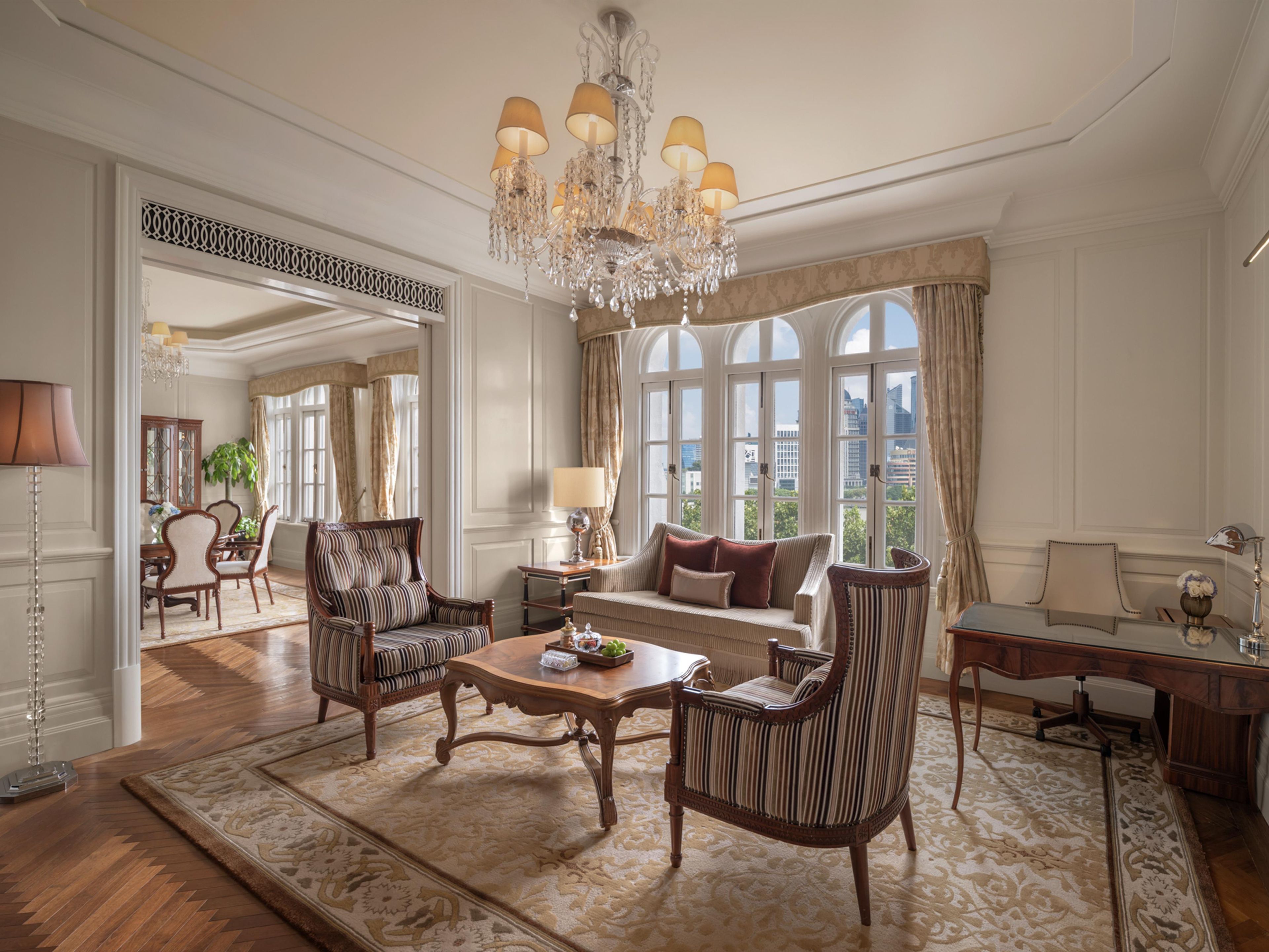A spacious living room with a chandelier, a sofa, armchairs, a coffee table, and a view through large windows.