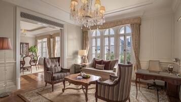 A spacious living room with a chandelier, a sofa, armchairs, a coffee table, and a view through large windows.