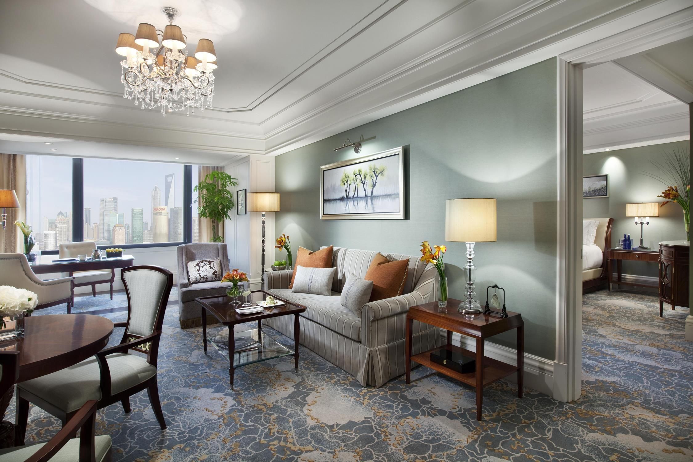 Une chambre d’hôtel avec vue sur la ville, un lustre, un canapé, une table à manger et une grande fenêtre.