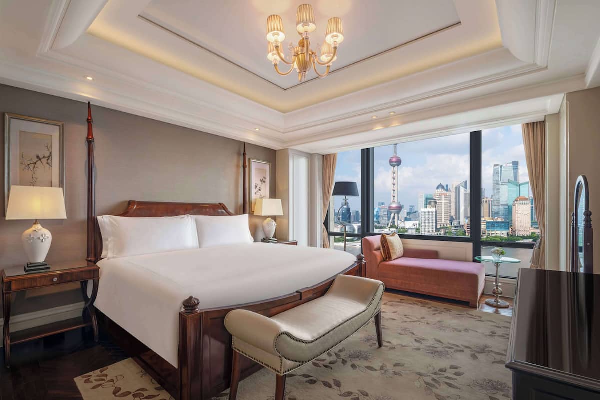 Ein geräumiges Hotelzimmer mit einem großen Bett, einer Bank, einem Sofa und Blick auf die Skyline der Stadt.