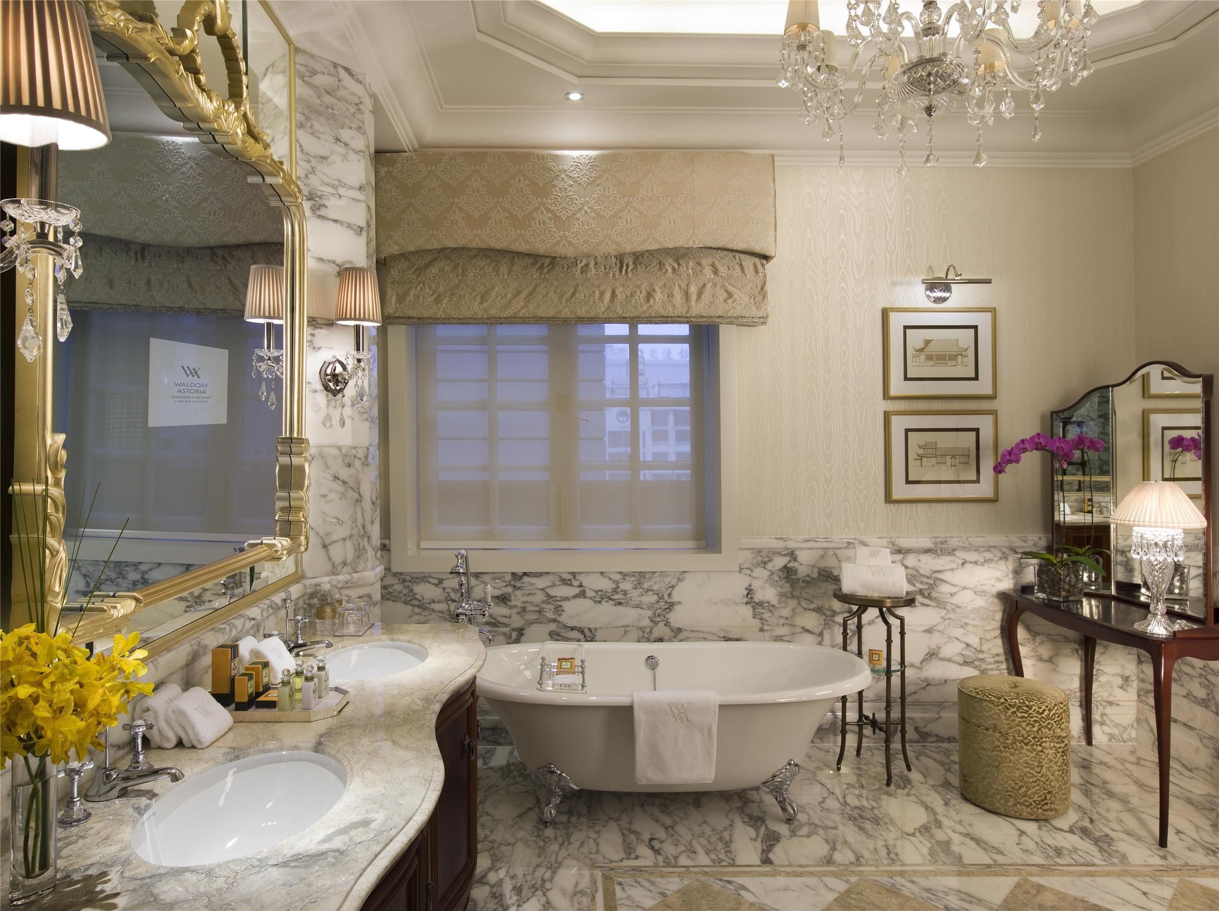 A luxurious bathroom with a large bathtub, two sinks, a vanity with a mirror, and a chandelier.