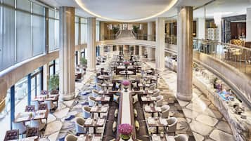 A spacious hotel lobby with a central seating area, a staircase, and a view of the outside.