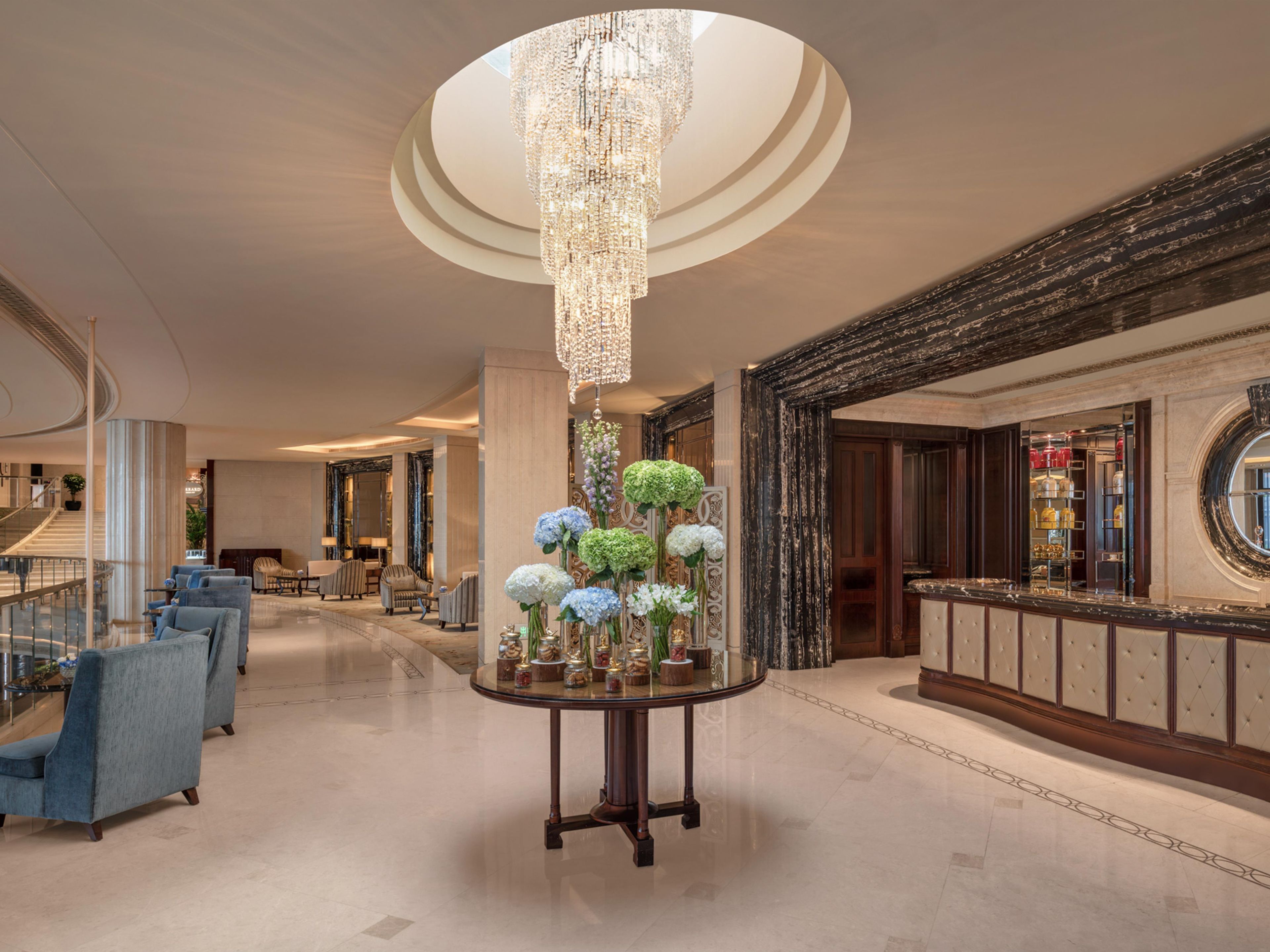 A lobby with a grand chandelier, a round table with floral arrangements, and a bar area with a circular mirror.