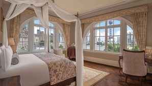 Un dormitorio amplio con una cama grande, un espacio para sentarse y vistas a la ciudad a través de amplios ventanales.
