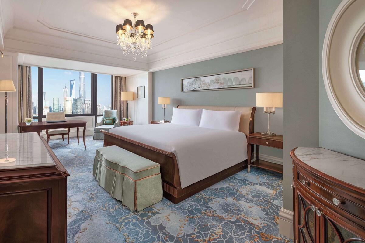 Une chambre d’hôtel avec un grand lit, un bureau, une chaise, une petite table et une vue sur les toits de la ville.