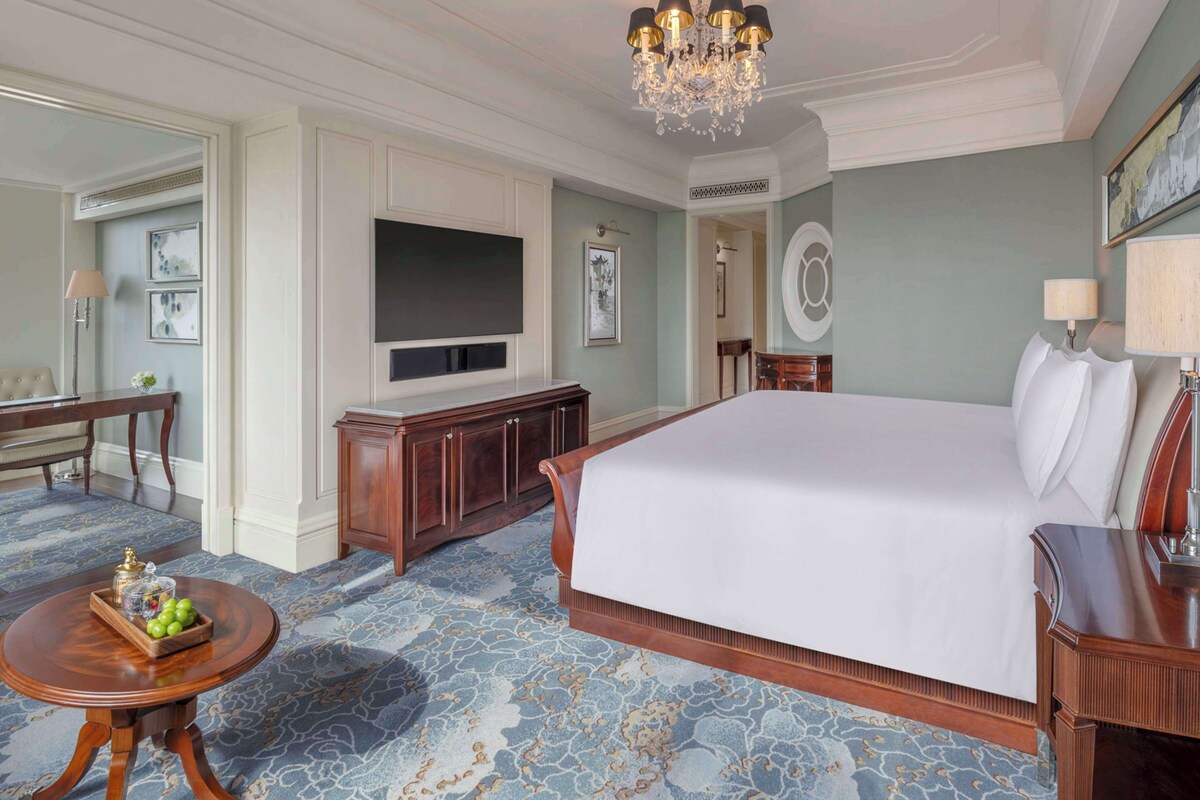 Une chambre d’hôtel spacieuse, dotée d’un grand lit, d’un téléviseur fixé au mur, d’un bureau en bois et d’un lustre.