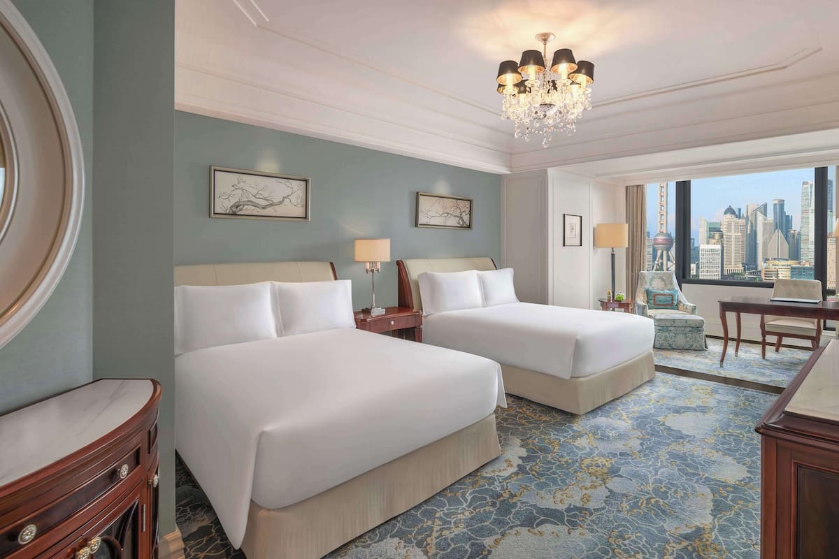Ein Hotelzimmer mit zwei Betten, einer Kristallleuchter, Kunstwerken an den Wänden und Blick auf die Stadt.