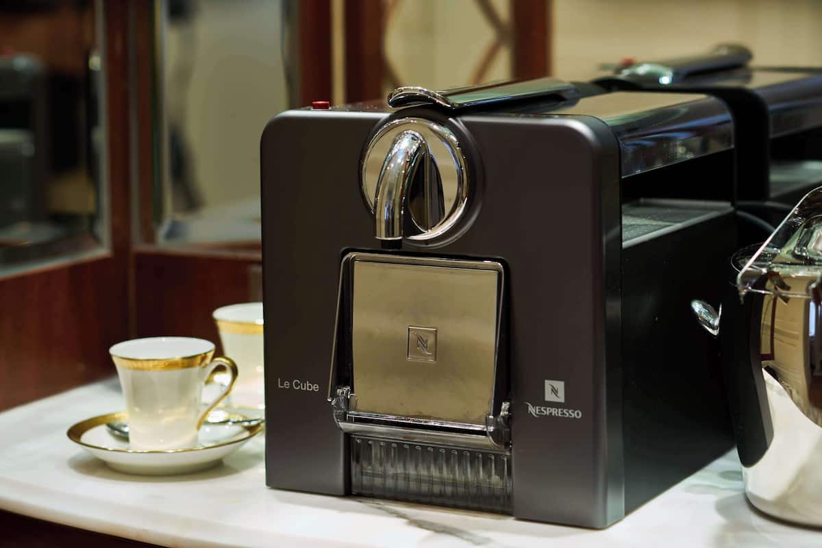 Eine altmodische Espressomaschine mit vergoldetem Griff und einer Glasscheibe, platziert auf einem weißen Tablett mit einer goldfarbenen Tasse und Untertasse.