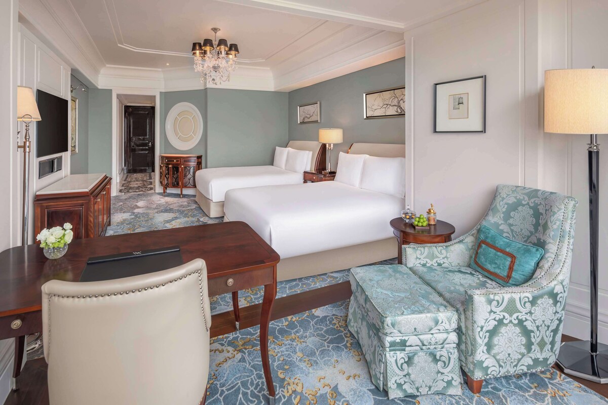 Une chambre d’hôtel avec deux lits, un bureau, une chaise, un lustre et une moquette à motifs.