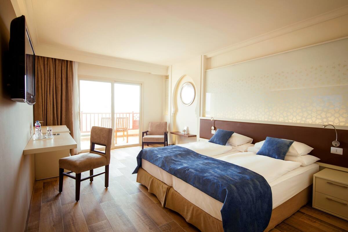 Quarto de hotel com cama, escrivaninha, cadeira e varanda.