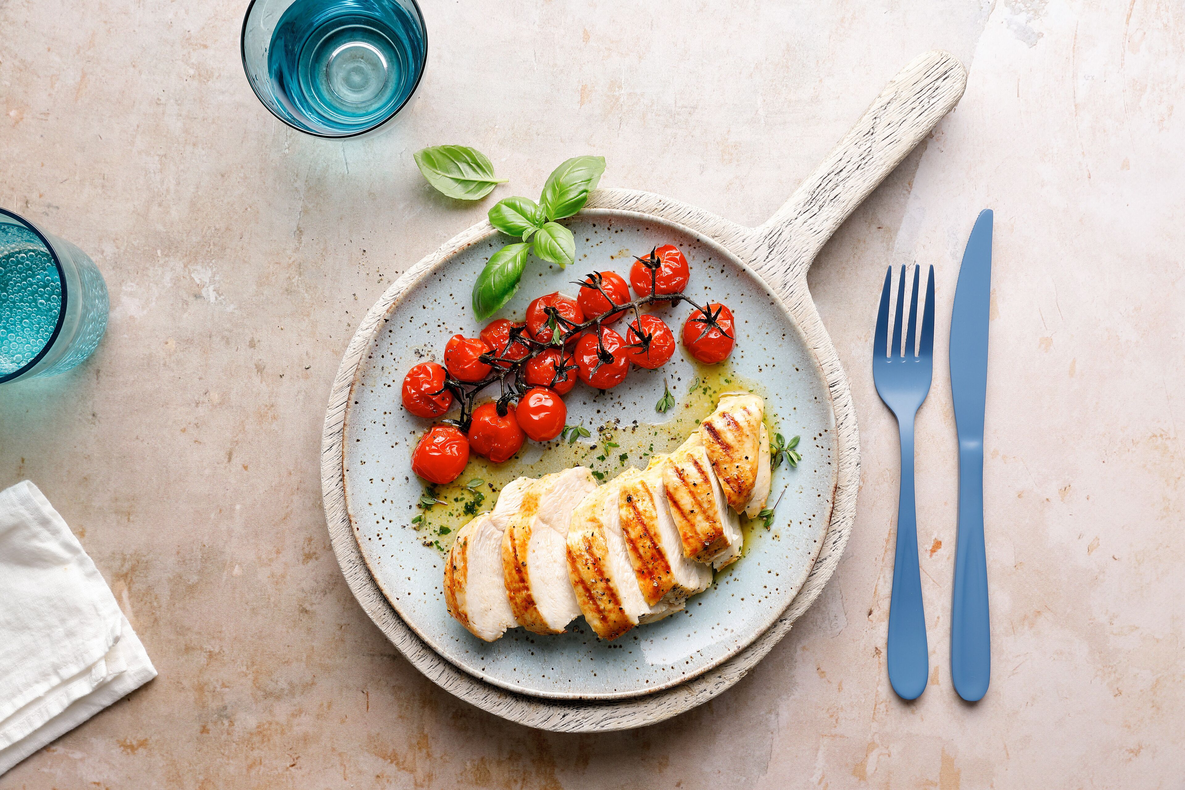 A plate with grilled chicken, cherry tomatoes, and basil on a textured surface.